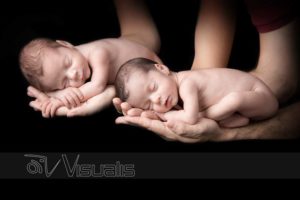 Gemelli neonati addormentati sopra le mani dei genitori su sfondo nero