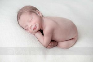 neonato rannicchiato a pancia in giú su tessuto bianco