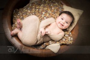 bambina sorride avvolta in sciarpa beige dentro cestino di legno
