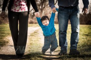 Bambino cammina su sentiero preso per mano dai genitori